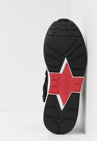 Sneakersohle mit schwarzem Gummibasis, rotem und weißen Akzent in Sternform, strukturierten Oberfläche mit standardisiertem Profil.