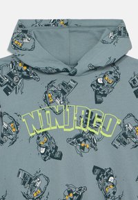 Szürke kapucnis pulóver, amelyen a Ninjago karakterek különböző pózokban láthatók, kiemelkedően sárga "NINJAGO" logóval. Puha pamutból készült, sima tapintású.