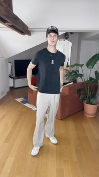 Must mets mustaga T-särgiga, valge tekstiga, heledate triibuliste pükste ja valgete tossudega. Taustal on diivan ja pottiorhidee.