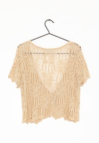 Top de encaje beige con un ajuste holgado, mangas cortas y un dobladillo en forma de ondas. Presenta un patrón intrincado con un diseño de tejido abierto.