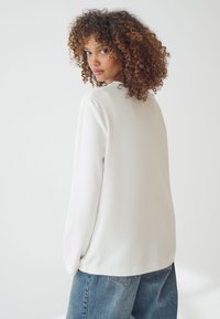 Maglietta a maniche lunghe di colore avorio, dal taglio morbido e dalla texture liscia, con scollatura rotonda, abbinata a jeans in denim blu a vita alta.