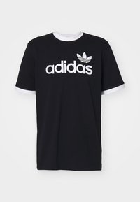 Svart bomullströja med vit rundhals och ärmar. Har en stor vit "adidas"-logotyp och den ikoniska trefoil-designen på framsidan.