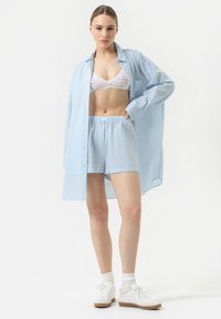 Chemise rayée bleu clair, bralette en dentelle blanche et short assorti. Baskets blanches avec semelles en caoutchouc et chaussettes blanches retroussées. Tenue décontractée.