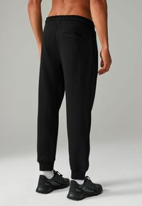 Pantalones de chándal negros con cintura elástica, que presentan un bolsillo trasero. El material parece suave, con puños acanalados en los tobillos.