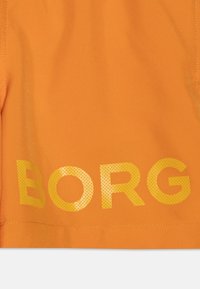 Oranžová látka s veľkým žltým bodkovaným textom "BORG" na spodnej strane; hladká textúra, ležérny dizajn a pevné švy.