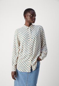 Long-sleeve, button-up shirt in cream with a diamond pattern in teal and light yellow. Soft fabric with a collared neckline and relaxed fit.
