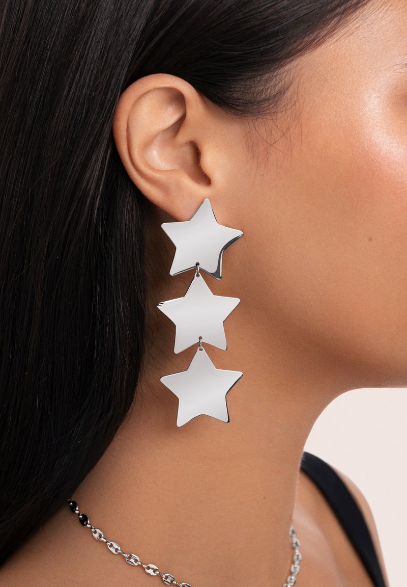 Pendientes en tono plateado con tres formas de estrella apiladas, con un acabado suave y reflectante y un diseño liviano. Apta para diversas ocasiones.