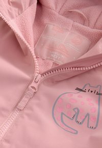 Rosa wasserdichte Jacke mit einem plüschigen Innenfutter, ausgestattet mit einem Frontreißverschluss und einer Katzengrafik mit pinken Punkten. Das Etikett weist auf geklebte Nähte hin.