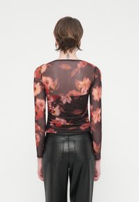 Top din plasă cu mânecă lungă, cu un model floral întunecat în nuanțe de roz și portocaliu, având un design strâns și decolteu din dantelă. Asortat cu pantaloni negri.