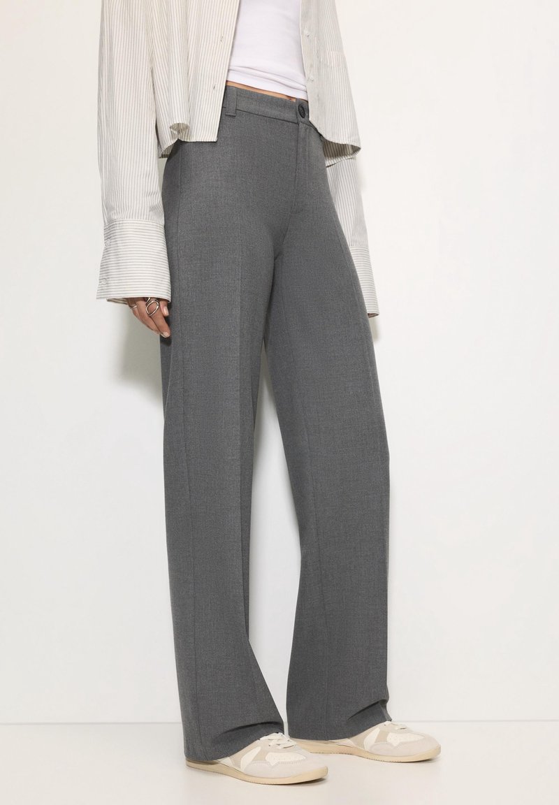 Personne portant un pantalon gris à jambes larges, des baskets blanches, un top court blanc et une chemise rayée à manches longues avec des poignets surdimensionnés.