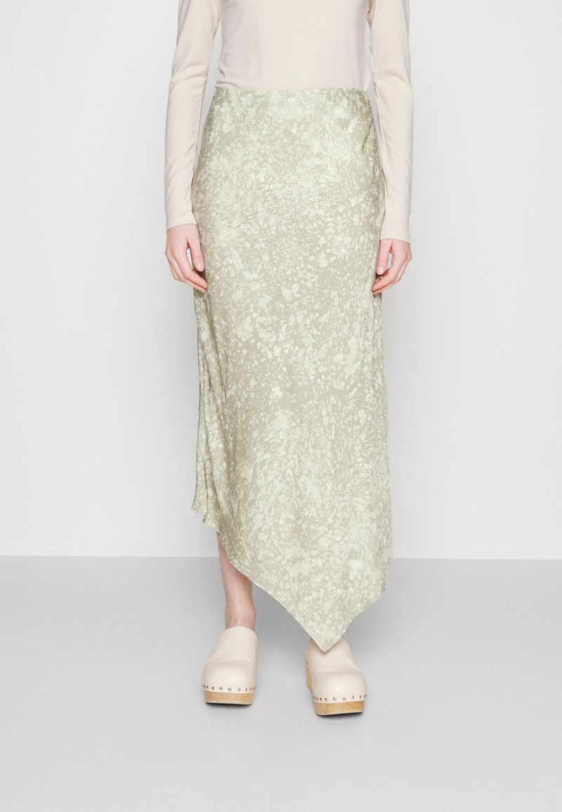 Ανοικτό πράσινη ασυμμετρία φούστα με υφή, με ελαφρώς φρουτημένο στρίφωμα, σε συνδυασμό με μπεζ ξύλινες καλτσοβαρές.