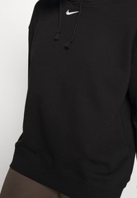 Svart Nike-hoodie med dragsnodd och en liten vit logotyp på bröstet. Har en avslappnad passform och mjuk tygtextur.