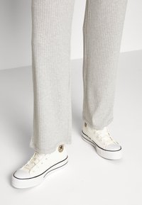 Ljust grå ribbad byxor i kombination med vita kanvas sneakers som har svarta accenter och en logolapp på sidan.