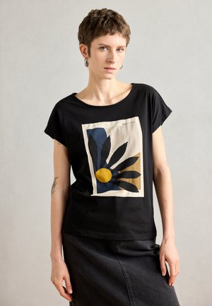 Schwarzes T-Shirt mit einem bedruckten Design mit blauen Blättern und einem gelben Kreis auf einem beigen Hintergrund. Weicher Stoff, lässiger Schnitt, kurze Ärmel.