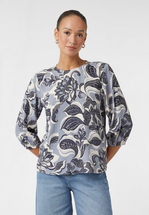 Blouse à motifs floraux en bleu doux et crème, présentant un design complexe en marine, un col rond et des manches bouffantes trois-quarts.