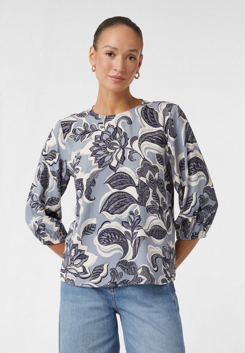 Bluse mit floralen Mustern in sanftem Blau und Creme, mit einem kunstvollen Design in Marineblau, runder Brustlinie und dreiviertellangen Puffärmeln.