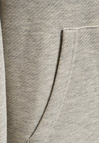 Nærbillede af lysegråt stof med en diagonal lomme syet ind i blødt, tekstureret strikmateriale.