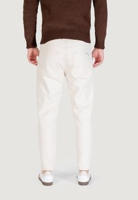 Pantaloni in denim bianco con una vestibilità affusolata, dotati di tasche posteriori e una lunghezza sopra la caviglia, abbinati a sneakers bianche e un maglione in maglia marrone.