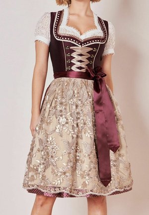 Kvinde iført en traditionel brun og beige dirndl-kjole med blomsterbroderi, blonderbluse, krydset livstykke og en satin sløjfe bundet i taljen.