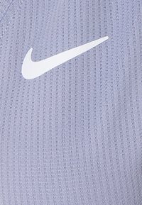 Tela deportiva Nike de color púrpura claro con un patrón texturizado; presenta un prominente logo blanco de Nike Swoosh en la superficie.