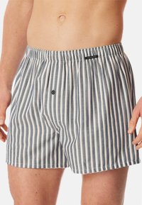 Boxers en coton rayés avec une taille élastique, présentant des rayures verticales bleues et blanches et un petit logo brodé à l'avant.