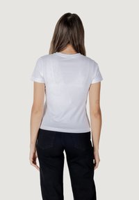 Witte shirt met korte mouwen en een ronde hals, gladde textuur en subtiele patroondetails op de achterkant, gecombineerd met zwarte broek.