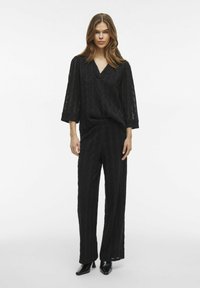 Completo nero a due pezzi composto da un top ampio e strutturato con scollatura a V e maniche a 3/4, abbinato a pantaloni dritti con un motivo simile.