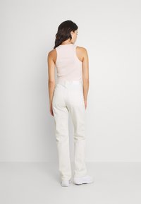 Top de alças rosa claro com design sem mangas, combinado com calças brancas de cintura alta, apresentando bolsos visíveis e passadores de cinto.