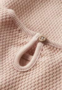 Nahaufnahme von pinkem Strickstoff mit einem runden Ausschnitt, der mit einem gerippten Saum und einem kleinen Holzknopf zum Verschließen versehen ist.