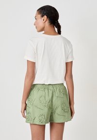 T-shirt en cotton blanc à manches retroussées associé à un short vert orné de motifs floraux brodés et de détails en œillet.