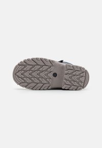 Semelle en caoutchouc gris avec un motif de bande de roulement en zigzag, comportant des tailles et des détails techniques en relief. Conçue pour l'adhérence et la durabilité.