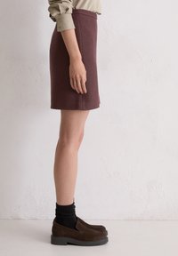 Bordeaux wollen rok met een rechte snit, met een middelhoge taille en een gladde textuur, gecombineerd met donkerbruine loafers en zwarte sokken.