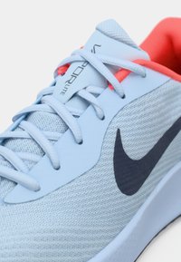 Pantofii sport de culoare albastru deschis, cu un superior din plasă respirabilă, logo-ul swoosh de culoare navy, accentuați cu detalii corai pe limbă și șireturi.