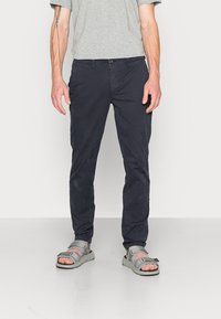 Pantalons slim-fit bleu marine en tissu doux, avec une fermeture à bouton et des poches. Associés à des sandales grises à bout ouvert avec des sangles réglables.