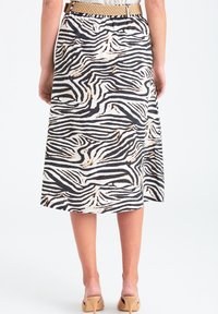 Kvinna iklädd en knälång zebra mönstrad kjol med ett beige bälte och naken högklackade mules, stående mot en vit bakgrund.