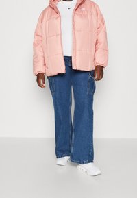 Rosa vadderad jacka med huva, med en framdragbar dragkedja och elastiska ärmslut, lager på lager över en vit t-shirt och tillsammans med blå utsvängda jeans.