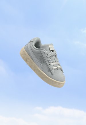 Baskets Puma gris clair avec semelle et lacets blancs flottant sur un fond de ciel bleu.