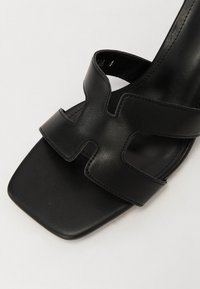 Sorte lær høye hælsandaler med firkantet tå, med en strukturert X-formet stroppedesign og jevn tekstur.
