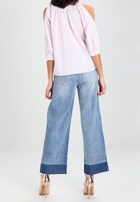 Vaaleanpunainen olkapäät paljastava paita, jossa on löysät hihat, yhdistettynä leveälahkeisiin sinisiin farkkuihin, joissa on tummempi helma. Asusteena beigellä sävyllä varustetut korot.