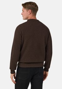 Hnědý pletený svetr s volným střihem, žebrovanými manžetami a lemem. Design zahrnuje kulatý výstřih a hladkou texturu. Nosit černé džíny.