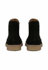 Bottes de cheville en daim noir avec une semelle en caoutchouc brun lisse et une doublure en cuir tan. Présente des coutures minimales et une silhouette épurée.