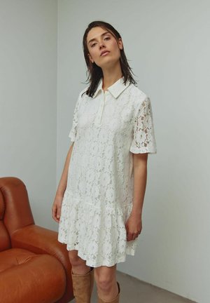 Blondekjole i hvid med kraveudskæring, korte ærmer og en skørt med vidde. Har blomsterprint og en løs pasform.