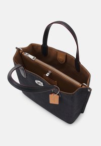 Sac cabas noir avec intérieur marron, anses en cuir, compartiment zippé, fermeture pression, et petite étiquette de marque en cuir sur une chaîne.