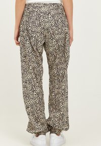 Zwarte en beige gemêleerde wijde broek met elastische tailleband, voorzien van dierenprint en cinched cuffs. Gecombineerd met witte schoenen.