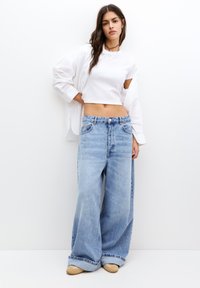 Lichtblauwe wijde spijkerbroek van denim, met een hoge taille, voorzakken en een vervaagde afwerking. Gecombineerd met een simpele witte crop top.
