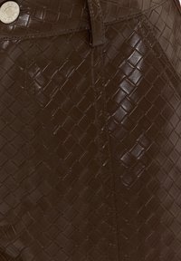 Surface en cuir brun foncé avec texture tissée et un bouton en argent visible sur un détail de rabat cousu.