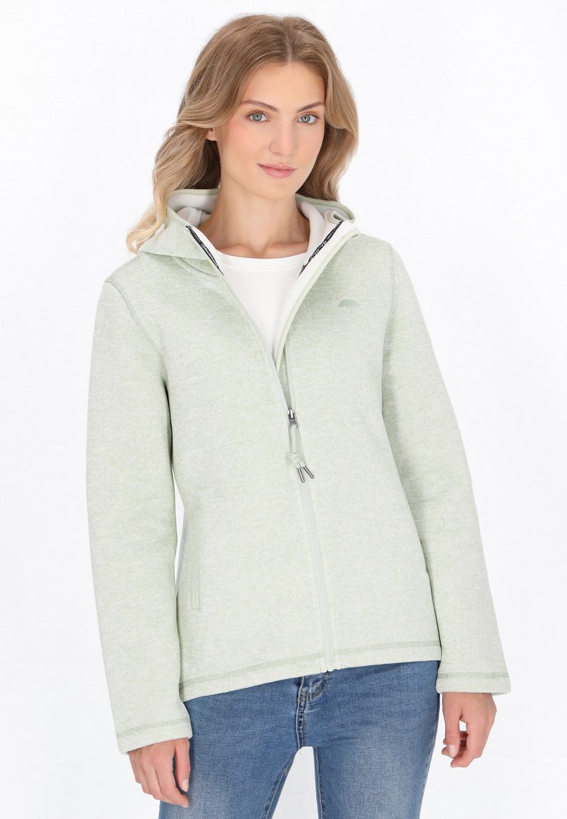 Jasnozielona kurtka z suwakiem wykonana z teksturowanej tkaniny, z kapturem, bocznymi kieszeniami i subtelnym logo. Nosi na sobie białą koszulę.