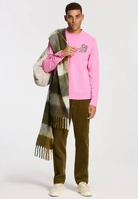 Cămașă roz cu mâneci lungi și logo, pantaloni de catifea cu dungi oliv, eșarfă în carouri verde și alb, și adidași crem. Ținută casual cu texturi stratificate.