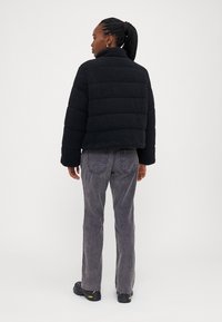 Svart fleece pufferjakke med høy krage, puffet design og ribbestrikkede mansjetter, kombinert med grå kordfløyelsbukser og svarte joggesko.