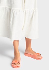 Des sandales à glissière de couleur pêche en caoutchouc lisse, dotées d'une large bride avec une boucle rectangulaire et d'une semelle rembourrée.